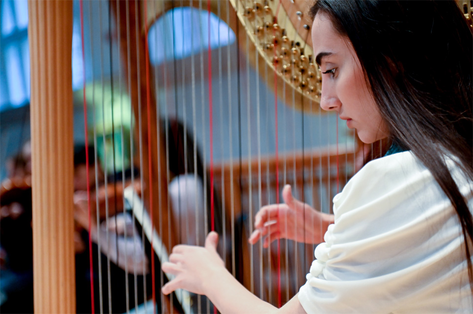 Female student playing the harp in an orchestra rehearsal.